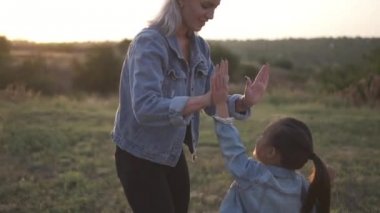 Yüksek beş Avrupa annesi ve çalışma düz için kameraya veren şirin küçük Çinli kız. Karışık yarış Aile, Avrupa anne ve Asyalı kızı vakit parkta sunset Bulvarında. Bahar ya da yaz sezonu sıcak. Ağır çekim vurdu
