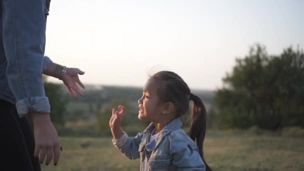 可爱的中国小女孩给她的欧洲母亲高五 混血家庭 欧洲母亲和亚洲女儿在日落时在公园里度过的时光 温暖的春天或夏季 — 图库视频影像