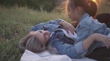 Karışık yarış Aile, Avrupa anne ve Asyalı kızı vakit parkta sunset Bulvarında. Onlar zemin gıdıklama birbirimize yalan ve gülümseyen oynamak. Bahar ya da yaz sezonu sıcak. B-roll yavaş vurdu