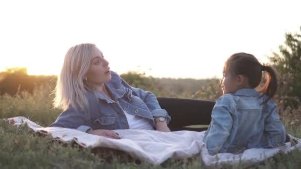 混血家族 ヨーロッパ母とアジア娘日没話してに公園で時間を過ごすと 笑顔します 暖かいばねまたは夏のシーズン — ストック動画