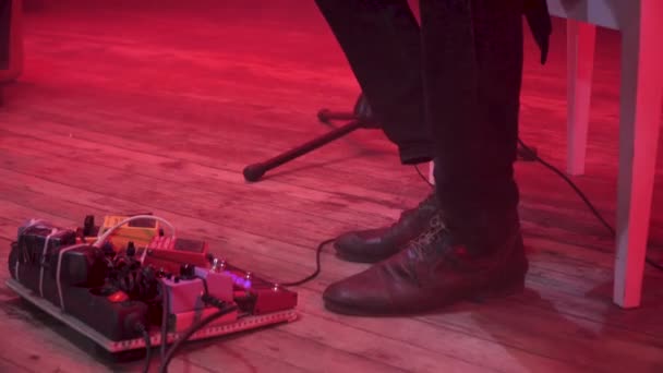 在背景上有红灯和烟雾的音乐表演中 吉他手改变了踏板上的效果踏板上的声音效果 他的脚踩在舞台地板上 — 图库视频影像