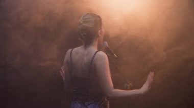 Duygusal müzik grubu ile Derma ışık ve arka plan üzerinde duman ile sahnede performans kız şarkıcı etrafında sinek Stedicam. Parlak konser sahne ışıkları, duman ve sis