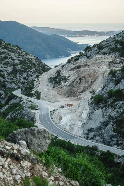 El sinuoso camino conduce a través de las montañas más allá de la minería de granito. Una hermosa vista de las montañas del cielo del atardecer y el mar es visible en la distancia —  Fotos de Stock