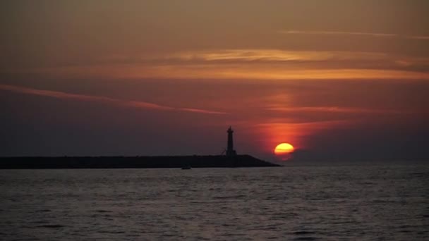 ボートのシルエットは灯台のそばの海の夕日に浮かんでいます — ストック動画