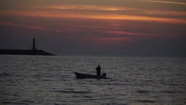 ボートのシルエットは灯台のそばの海の夕日に浮かんでいます — ストック動画