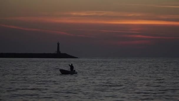 ボートのシルエットは灯台のそばの海の夕日に浮かんでいます — ストック動画