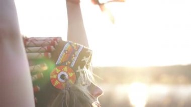 Kızılderili başlıklı güzel bir kız ve renkli makyajlı bir kostüm gün batımında elinde kızılderili otları tutuyor. Yan görünümü kapat