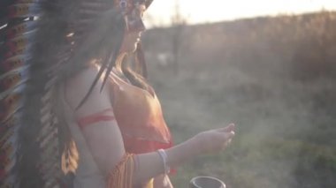 Amerikan yerlisi başlıklı güzel bir kız ve renkli makyajlı bir kostüm elinde bir kase tutuyor ve diğer elinden barutu döküyor.