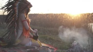 Amerikan yerlisi başlıklı güzel bir kız ve renkli makyajlı bir kostüm elinde havan topu, böğürtlen ve pudra ezer.