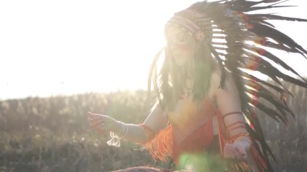 美しいです女の子でネイティブアメリカインディアンの頭と衣装でカラフルな化粧いくつかの儀式を行い 地面をスロー — ストック動画