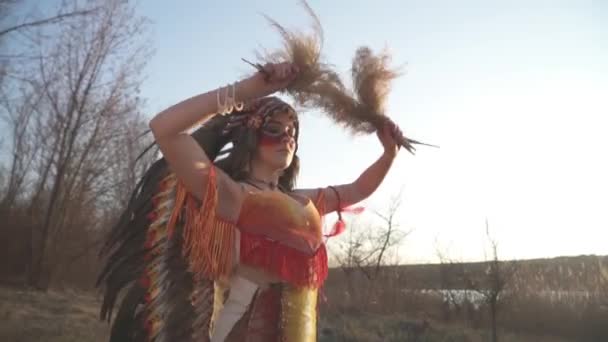在美国本土印第安人头饰和服装的美丽女孩 五颜六色的化妆 让一些仪式舞蹈与印度草在她的手中 山核桃属 — 图库视频影像