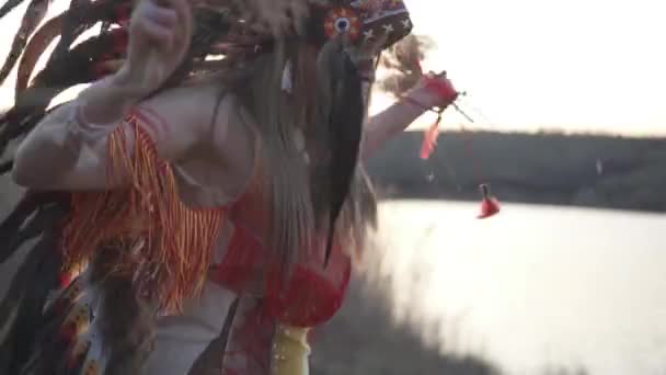 彼女の手にインド草と日没の儀式のダンスを実行カラフルなメイクアップとネイティブアメリカインディアンの頭と衣装で美しい女の子 ソルガストラム ナッツ — ストック動画