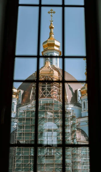 Window view of an unfinished church with a golden dome