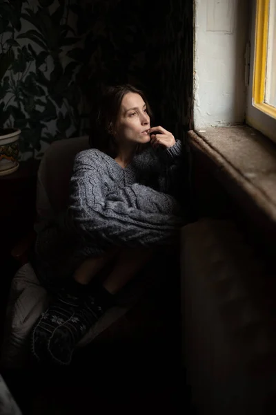 一个穿着灰色针织毛衣和保暖袜子的沉思女孩坐在椅子上 双腿交叉 望着窗外 — 图库照片