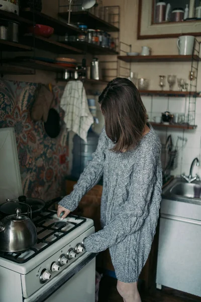 小女孩穿着一件灰色针织毛衣 在厨房的煤气炉上生火 免版税图库图片