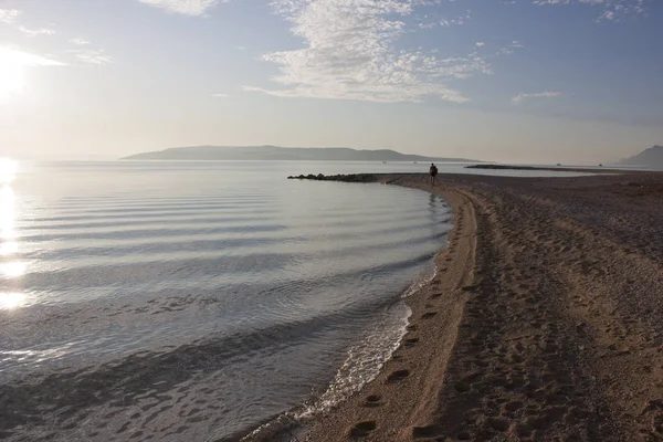 Gün batımında sutyen adasının yanındaki çakıl taşı plajı. Sakin deniz, yalnız adam yürüyor ve ayak izleri bırakıyor..