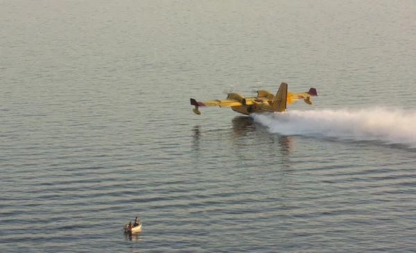 İtfaiyecilerin uçağı denizden su yüklüyor ve küçük bir tekneyle balıkçıların yanından geçiyor..