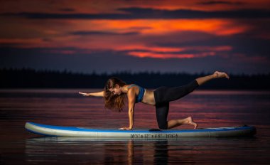 Doğal göl Velke Darko karanlık, renkli günbatımında paddleboard yoga egzersiz uzun kahverengi saçlı güzel ince uygun kız