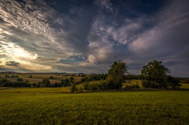 Güzel, güzel, yeşil çayır bulutlu mavi gökyüzü ve gün batımı arka planda ağaçlarda. Çek Cumhuriyeti Boskovice yakın