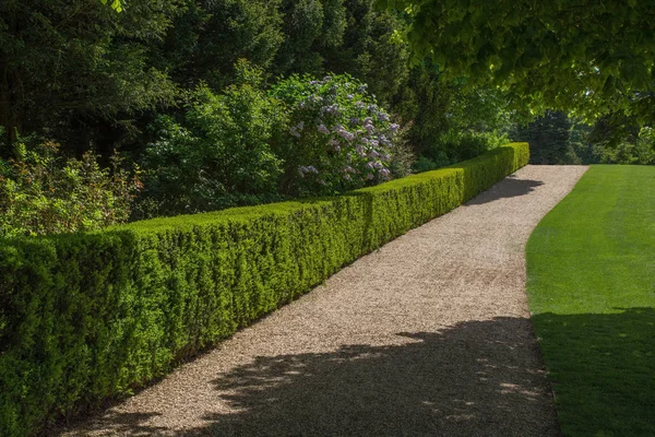Neat gravel path alonside a grass lawn and hedge in an English country house.