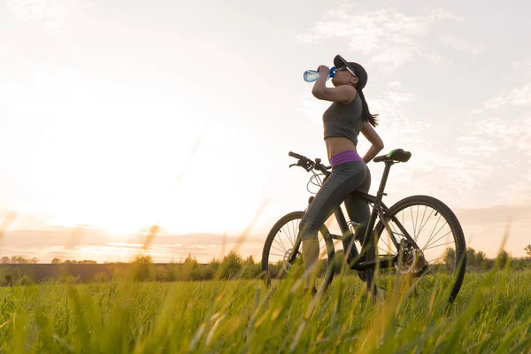 Pić wodę podczas treningów. Sportowe. kobieta na rowerze zachód słońca — Zdjęcie stockowe