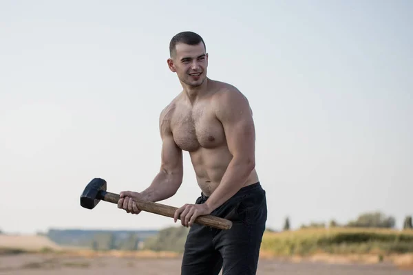 Sport Fitness Man Hitting Wheel Tire With Hammer. Sledgehammer Training. Young Healthy Guy. Outdoor Gym