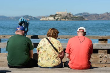 Ada ve Alcatraz hapishane içinde belgili tanımlık geçmiş Pier 39 San Francisco manzarası olan bir bankta oturan turist