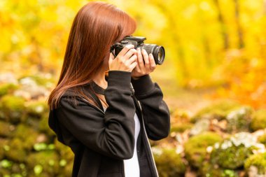 Kızıl saçlı Genç bir kadın bir ormanda bir refleks kamera ile fotoğraf çeker 