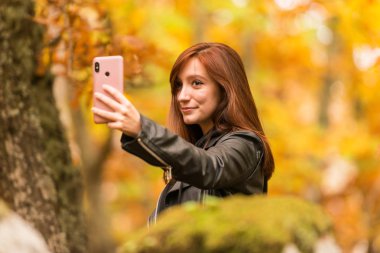 Kızıl saçlı Genç bir kadın ile cep telefonu ormandaki selfies yapıyor