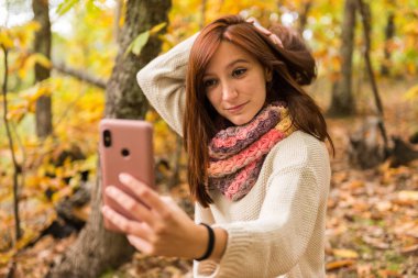 Kızıl saçlı Genç bir kadın ile cep telefonu ormandaki selfies yapıyor