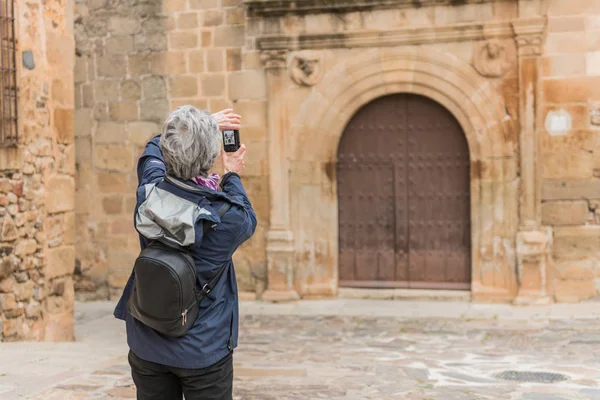 Egy idős asszony turizmus csinál vesz egy fénykép-ból egy régi ajtó a régi város Caceres, Extremadura, Spanyolország. — Stock Fotó