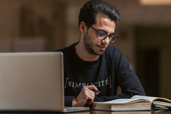 Jovem estudante de ciência da computação usa um laptop e um livro para estudar na Escola Politécnica de Cáceres, Espanha . — Fotografia de Stock