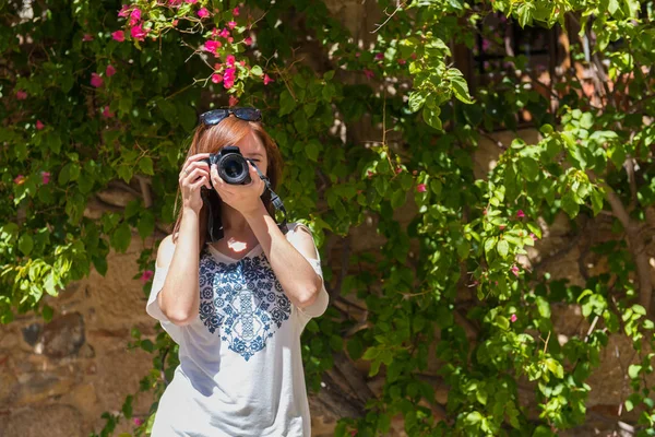 En ung kvinna med rödaktig hår tar fotografier med sin kamera bredvid en vägg täckt med bougainvillea Caceres — Stockfoto