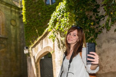 Genç bir kızıl saçlı turist Caceres eski kasabasında yeşil sarmaşık kaplı bir kule yanında bir selfie yapar