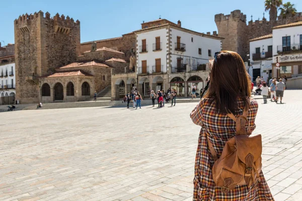 Bir sırt çantası ile genç bir kızıl saçlı turist Caceres Plaza Mayor fotoğrafları alır
