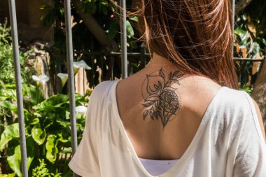 Arkadan bir Arum-Lily dövme ile genç bir kızıl saçlı turist Caceres aynı çiçekler ile bir bahçeye bakıyor