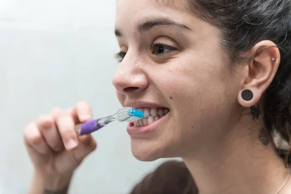 Young woman brushes her white teeth with a toothbrush.