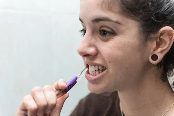 Young woman brushes her white teeth with a toothbrush.