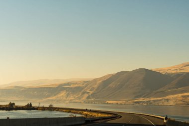 The US-30 highway passing by the Columbia River with water on both sides of the road near The Dalles clipart
