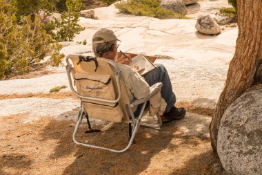 Katlanan sandalyede oturan bir adam Yosemite Ulusal Parkı 'ndaki Olmsted Point' te bir not defterine not alıyor.