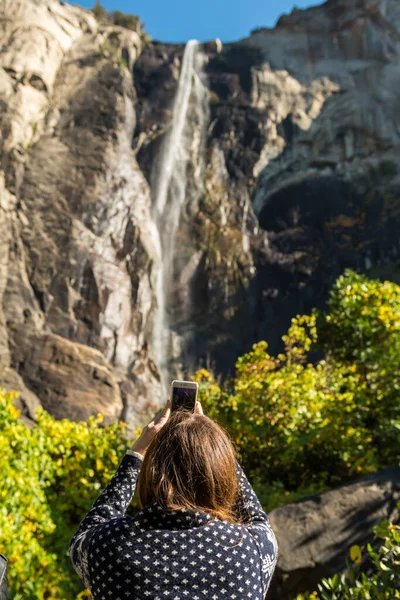 Una mujer toma fotos con su smartphone desde la base del Bridalveil Fall en el Parque Nacional Yosemite — Foto de Stock