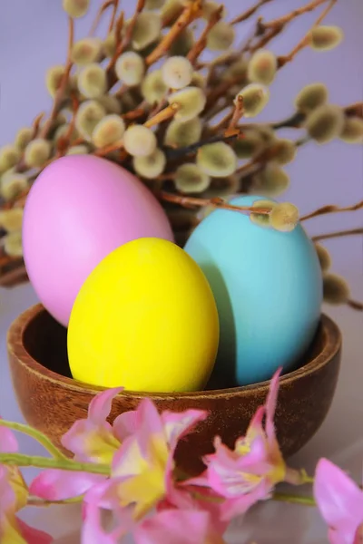 pink yellow blue eggs against background of willow and flowers for the Easter holiday