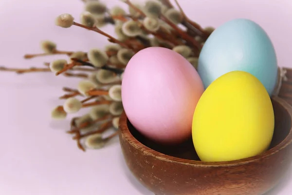 pink yellow blue eggs against background of willow and flowers for the Easter holiday