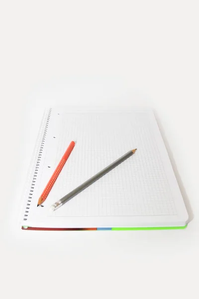 Lápices multicolores naranja verde gris sobre un cuaderno de fondo blanco —  Fotos de Stock