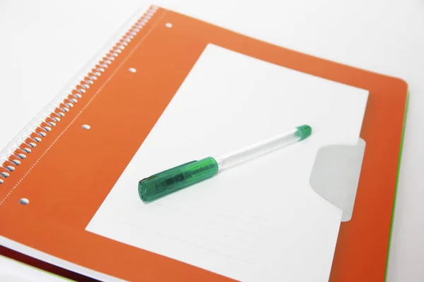 Zelená studentská pera na pozadí oranžového notebooku — Stock fotografie