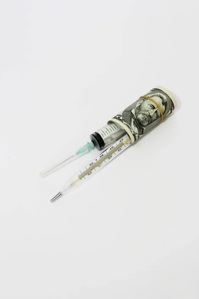 Seringa médica e termômetro em um rolo de dólares em um fundo branco — Fotografia de Stock