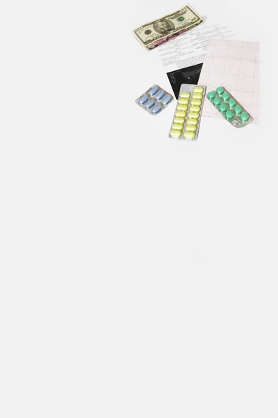 Dólares, comprimidos, cardiograma e uma consulta médica em fundo branco — Fotografia de Stock
