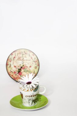 yeşil bir tabak üzerinde kahve demliği, beyaz bir arka plan üzerinde dekoratif desenli saat ve beyaz papatya çiçek