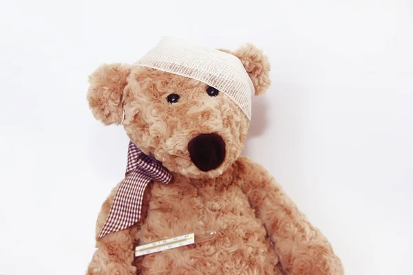 Miękki brązowy zabawka niedźwiedź chory z bandaż na głowie i termometr medyczny — Zdjęcie stockowe
