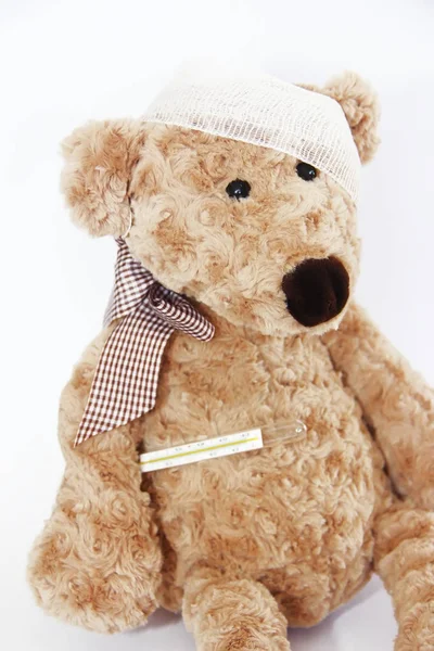 Soft brown toy bear sick with a bandage on his head and a medical thermometer — Stock Photo, Image